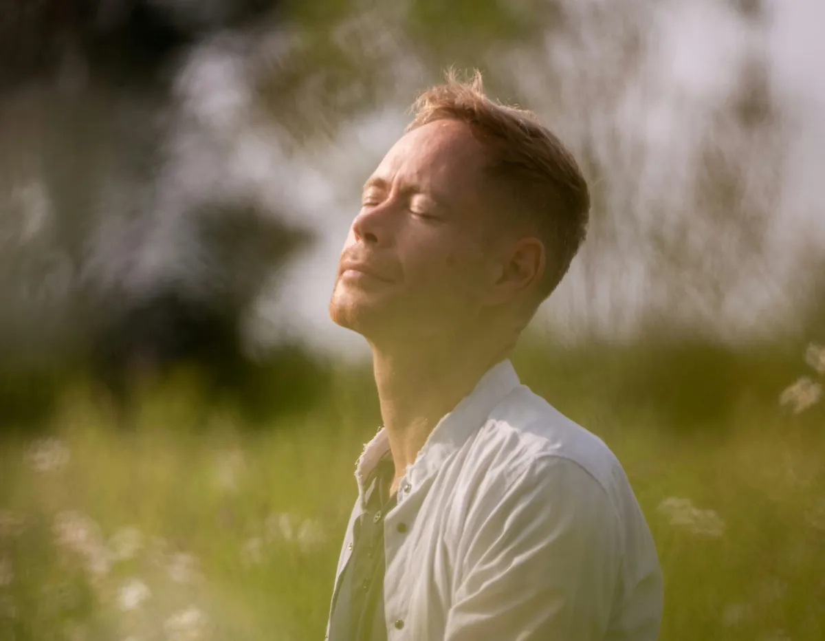Un homme les yeux fermés, le visage au soleil, dans les herbes hautes